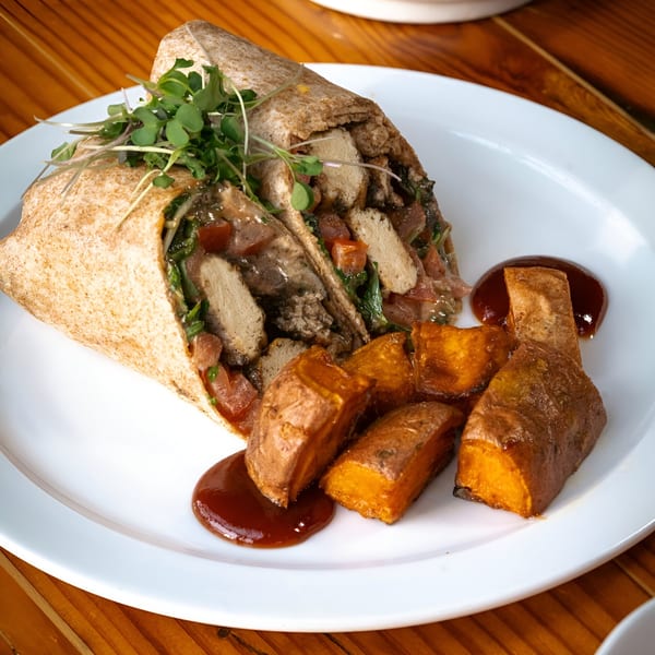Vegan wrap with microgreens, diced vegetables, and plant-based protein, served with roasted sweet potatoes and sauce.