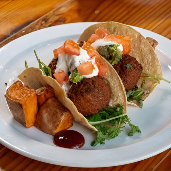 Vegan tacos with falafel, guacamole, tomatoes, and sour cream, served with sweet potato wedges.