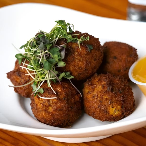 Majani Soulful Vegan Cuisine's crispy brown vegan hush puppies topped with microgreens and a side of sauce.