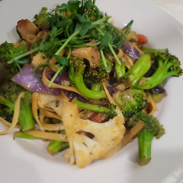 Vegan pasta dish with broccoli, cauliflower, red cabbage, and pea shoots in a white bowl.